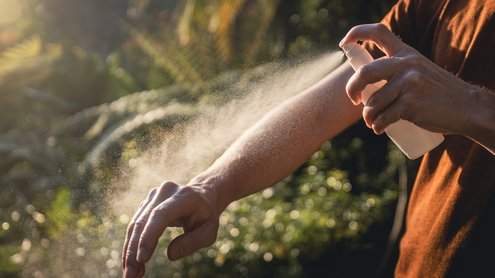 Person sprüht Spray auf die Haut.