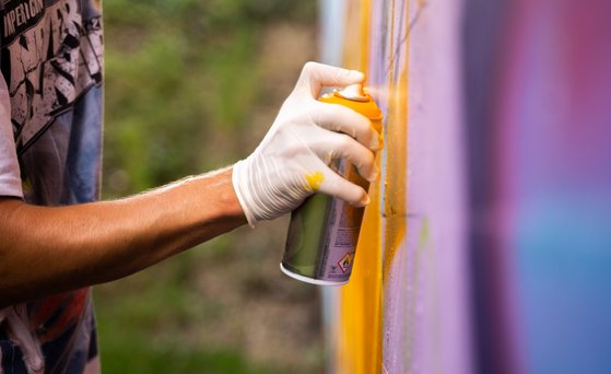 Chemikalien unter REACH Hand in weißem Handschuh hält Spraydose und sprüht mit gelber Farbe auf Graffitiwand.