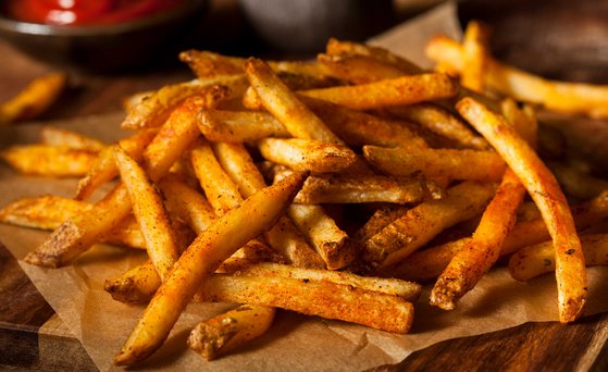 Pommes frites auf Backpapier, Nahaufnahme, Holztisch unscharf und im Anschnitt Schale mit Ketchup