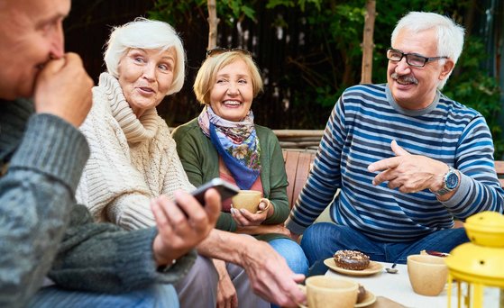 Seniorengruppe sitzt mit Tee und Kuchen draußen an einem Tisch und unterhalten sich.