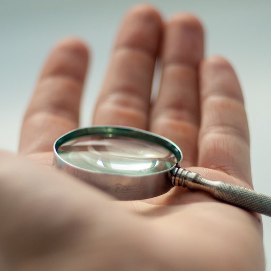 Kleine Lupe aus Metall liegt in einer Männerhand. Nahaufnahme.