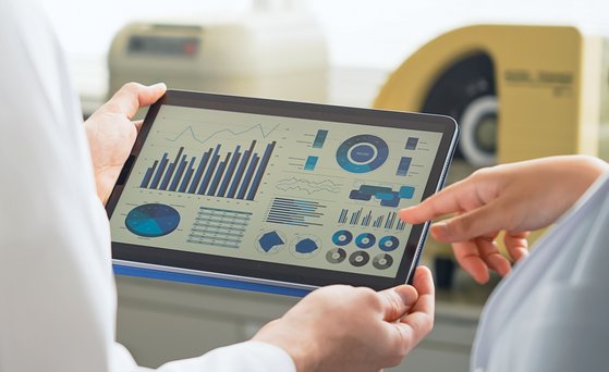 Tablet mit Diagrammen wird von zwei Personen im weißen Kittel gehalten.