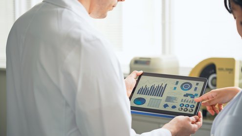 Tablet mit Diagrammen wird von zwei Personen im weißen Kittel gehalten.