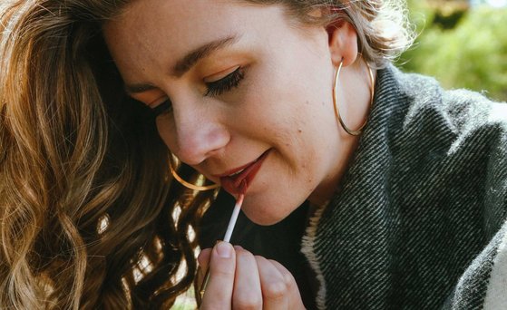 Kosmetische Mittel Frau trägt roten Lippenstift auf.