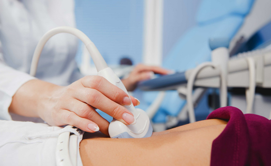 Expositionsstudien Person liegt auf dem Rücken und wird mit einem Ultraschallgerät am Bauch untersucht.