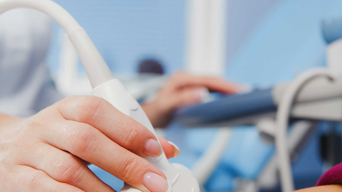 Person liegt auf dem Rücken und wird mit einem Ultraschallgerät am Bauch untersucht.