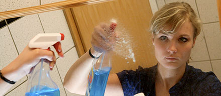 Eine Frau sprüht Glasreiniger auf einen Spiegel